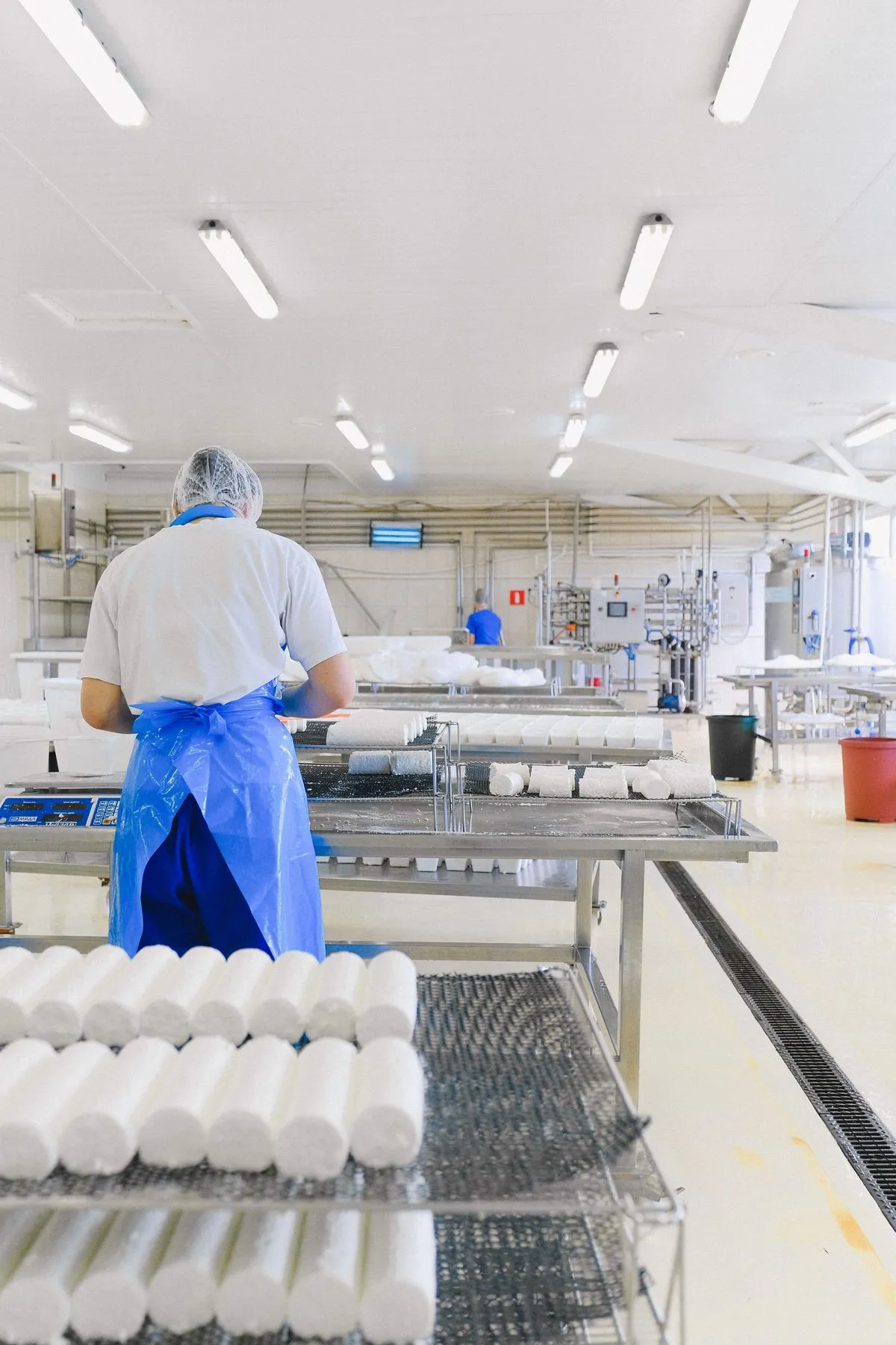 Atelier de production alimentaire aux sols et surfaces clairs, opératrice en tablier et charlotte.