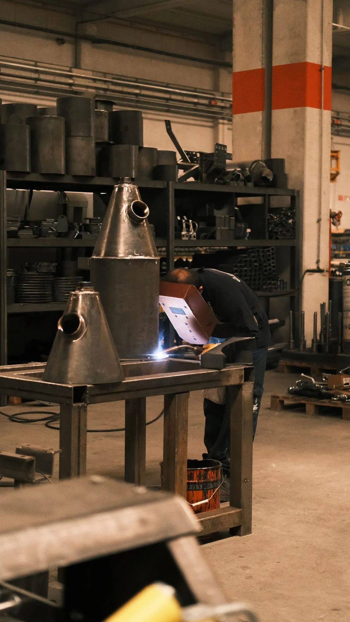 Soudeur au travail dans un atelier de fabrication métallique, pièces en acier sur l'établi.
