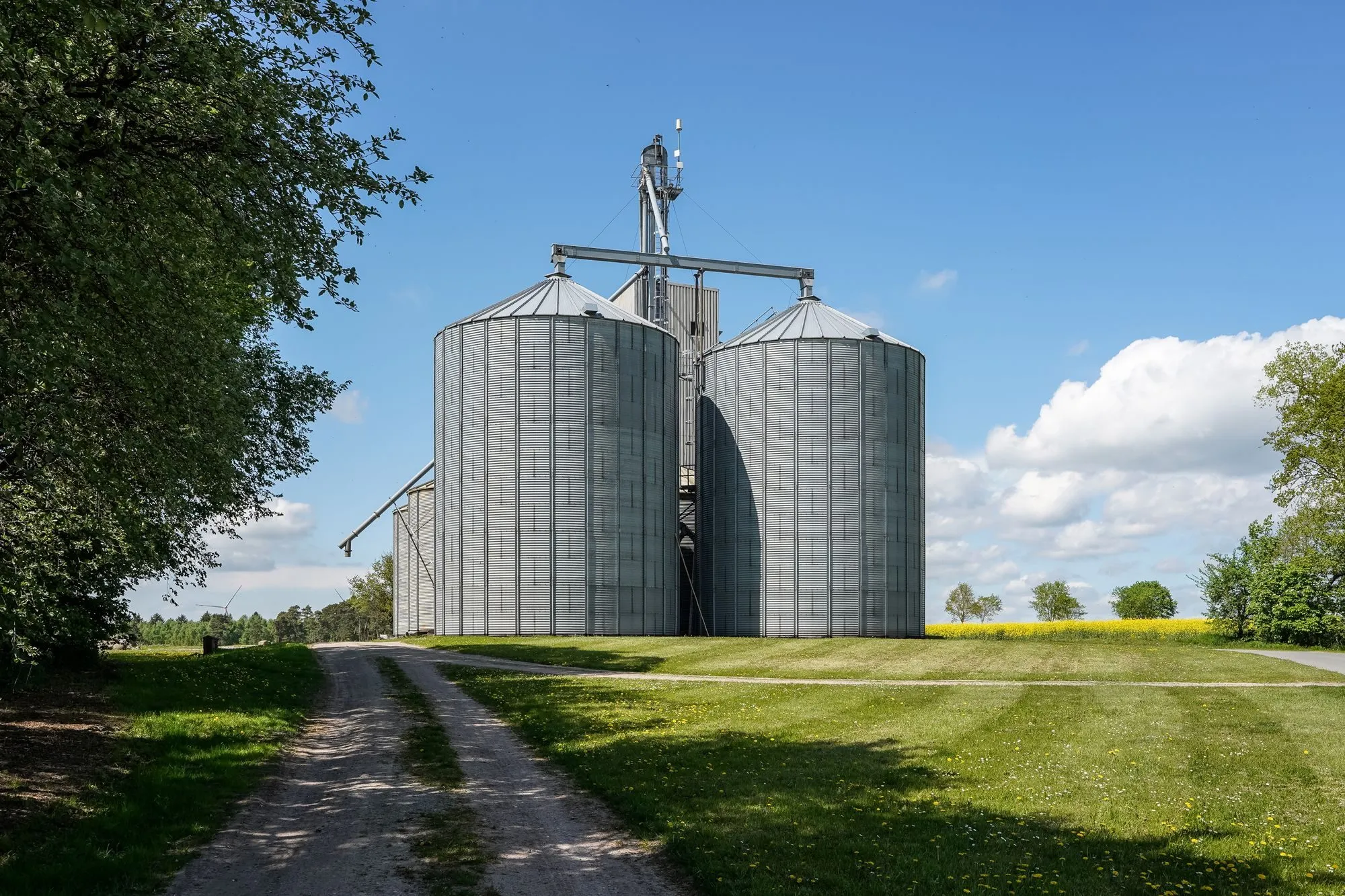 Deux silos métalliques dans un champ, sous un ciel bleu.